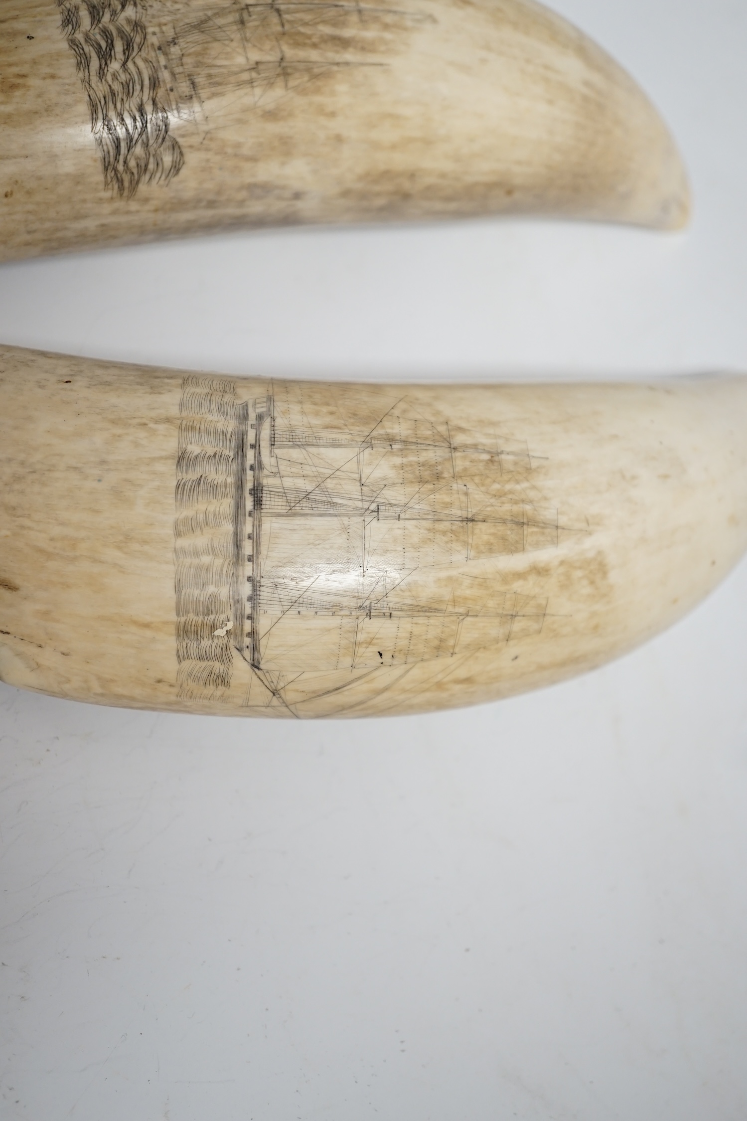 Two 19th century scrimshaw sperm whale teeth, each incised with a ship, 20cm in length